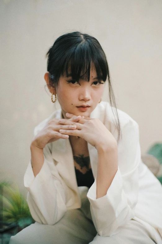 a woman sitting on top of a bed next to a plant, by Tan Ting-pho, unsplash, realism, white silky outfit, she has black hair with bangs, 🤤 girl portrait, long sleeves