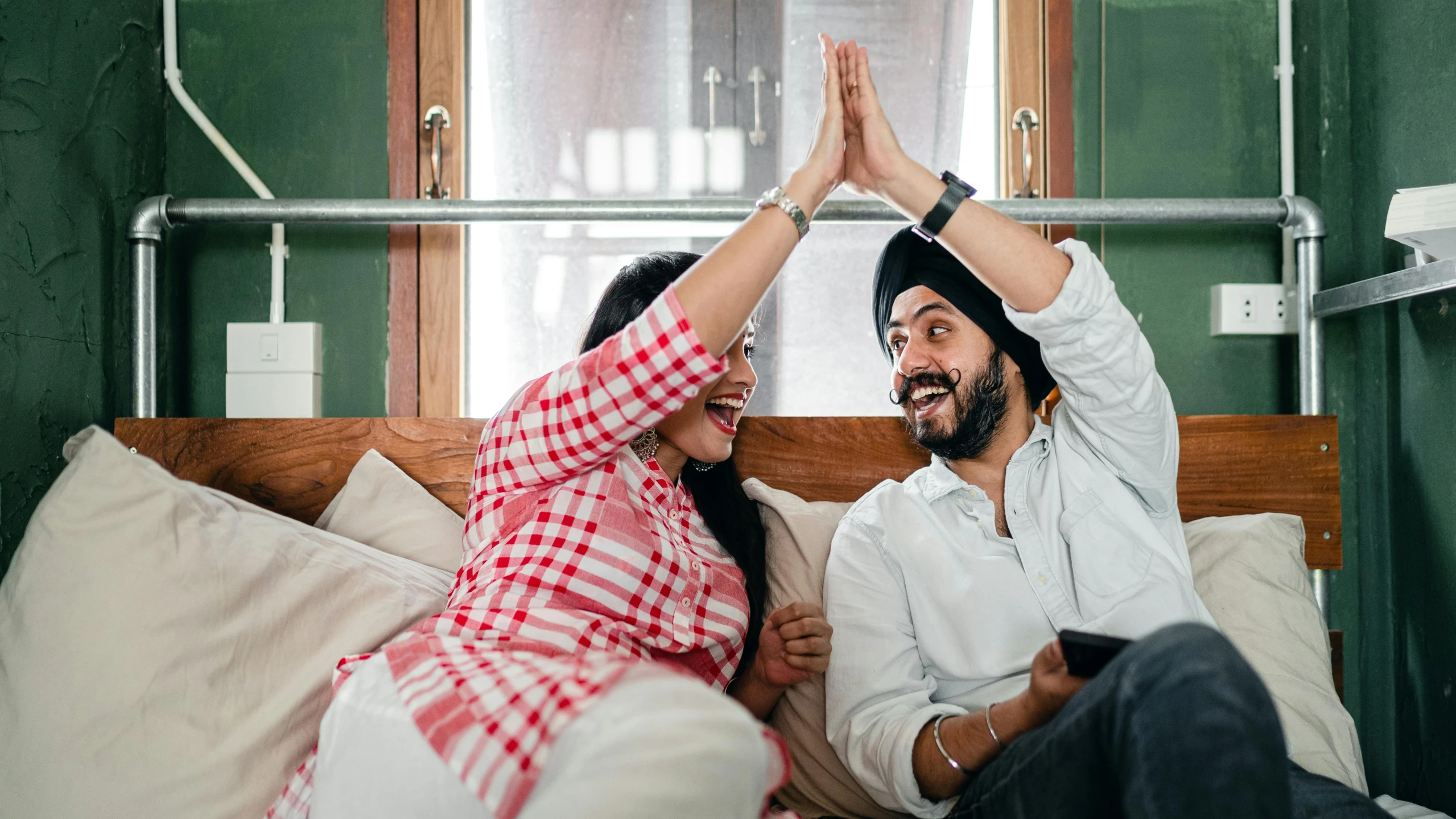 a man and a woman sitting on top of a bed, inspired by Manjit Bawa, pexels contest winner, waving and smiling, sitting on a couch, caps sideways, australian