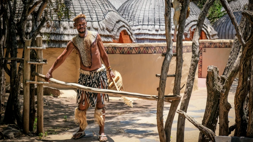 a man that is standing in the dirt, by Daniel Lieske, pexels contest winner, afrofuturism, thatched roofs, bushveld background, wearing an ornate outfit, waving arms