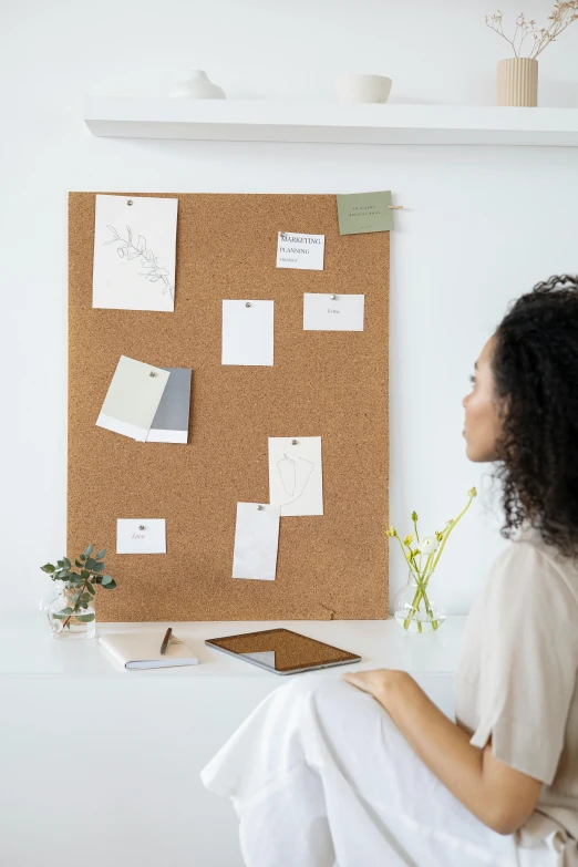 a woman sitting in front of a cork board, trending on pexels, on a white table, sustainable materials, 100lb cardstock, programming