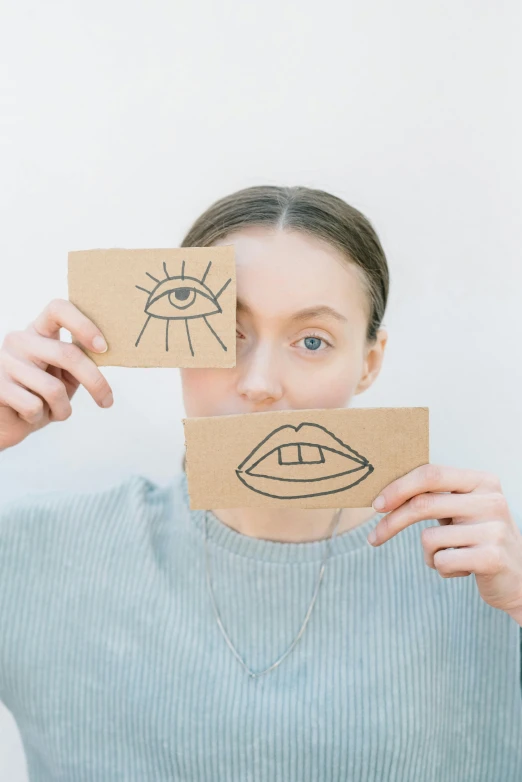 a woman holding two pieces of paper with eyes drawn on them, inspired by Man Ray, trending on pexels, many mouths, julia hetta, light eyes, drawn with a single line