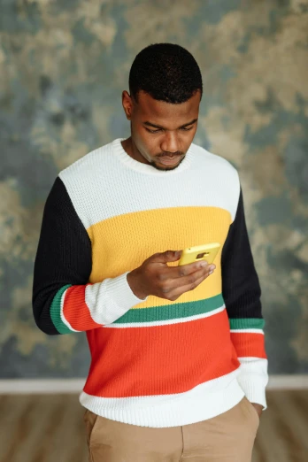 a man is looking at his cell phone, trending on pexels, renaissance, striped sweater, jamaican colors, color block, tall shot