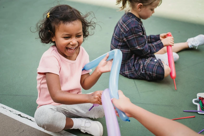 a group of children sitting on top of a tennis court, by Arabella Rankin, pexels contest winner, young girl playing flute, smiling and dancing, holding a balloon, balance beams