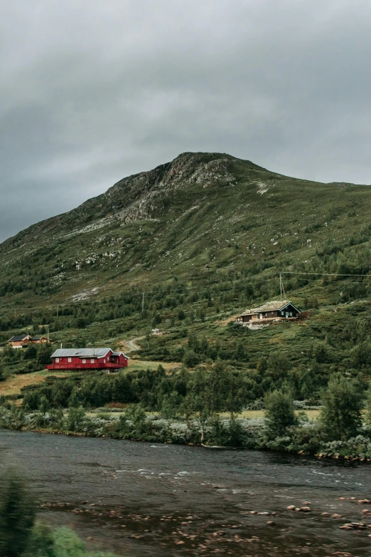 a red train traveling through a lush green hillside, by Roar Kjernstad, hurufiyya, building along a river, cottages, cinematic image, grey