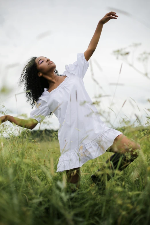 a woman in a white dress standing in a field, by Lily Delissa Joseph, pexels contest winner, playful pose of a dancer, tessa thompson inspired, black young woman, uncropped