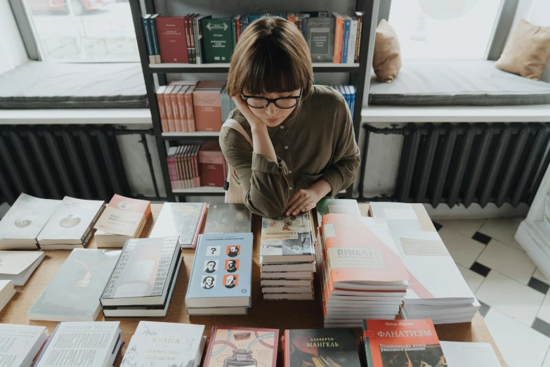 a woman sitting at a table with lots of books, pexels contest winner, pokimane, daniel clowes, many copies of them, vintage inspired