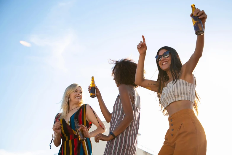 a group of women standing next to each other, trending on pexels, happening, holding a bottle of beer, yellow, on a hot australian day, people dancing