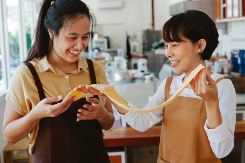 a couple of women standing next to each other, pexels contest winner, process art, golden ribbon, aussie baristas, wearing an apron, asian female