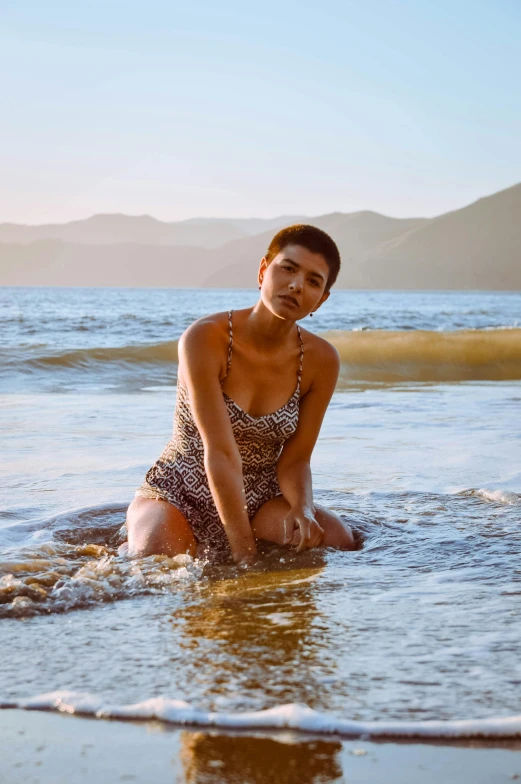 a woman sitting on top of a beach next to the ocean, “zendaya, nonbinary model, in the water, bay area