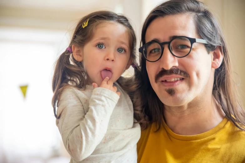 a man holding a little girl in his arms, an album cover, inspired by Leo Leuppi, pexels contest winner, with glasses and goatee, square nose, pokimane, jewish young man with glasses