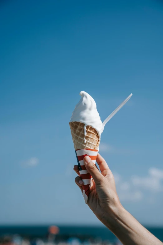 a person holding an ice cream cone on a beach, pexels, with a long white, hot food, sky blue, made of ice