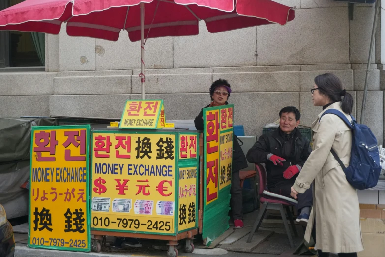a group of people sitting under a red umbrella, vending machine, lots of signs, korean woman, money