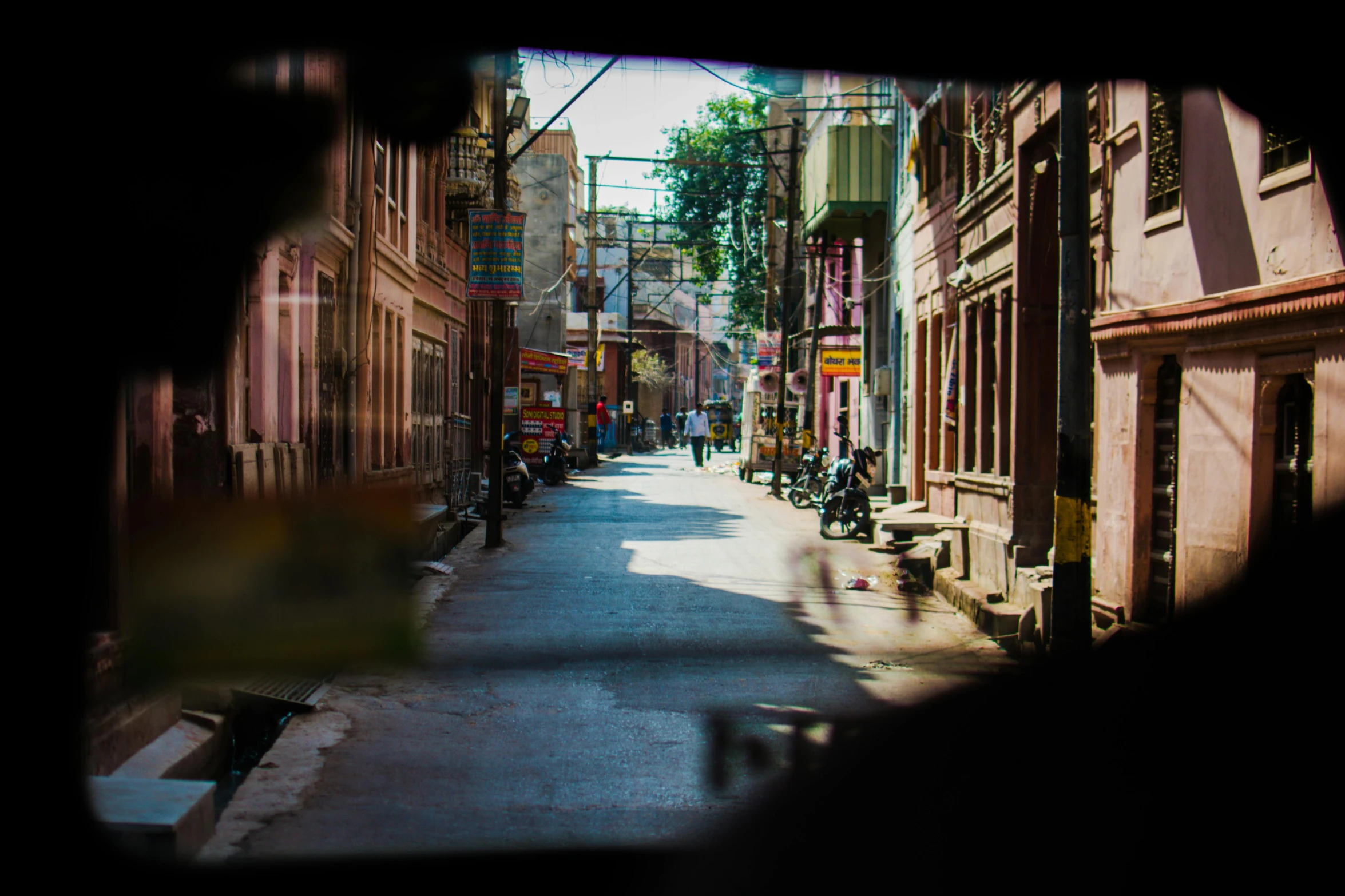 a view of a street through a hole in a wall, pexels contest winner, indore, with anamorphic lenses, shady alleys, view from a news truck