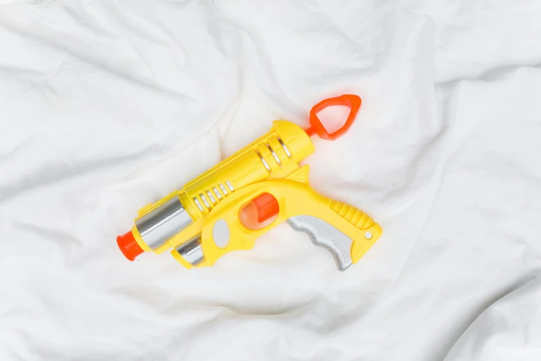 a yellow toy gun laying on top of a white sheet, holding a blaster, high quality product image”, zoomed out shot, a brightly coloured