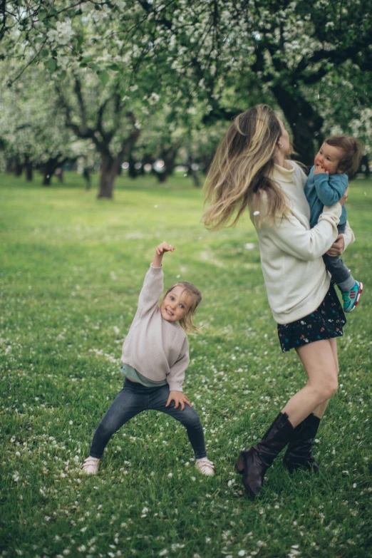 a woman holding a child in a park, pexels contest winner, around tree babies running, a blond, in a grass field, threes