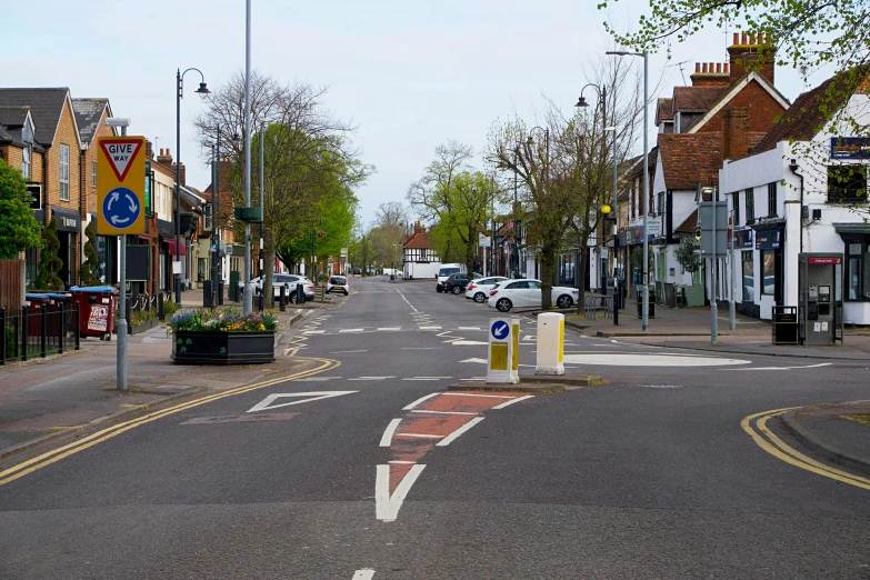 a street filled with lots of traffic next to tall buildings, by David Donaldson, unsplash, esher, quaint village, empty road in the middle, photograph of april