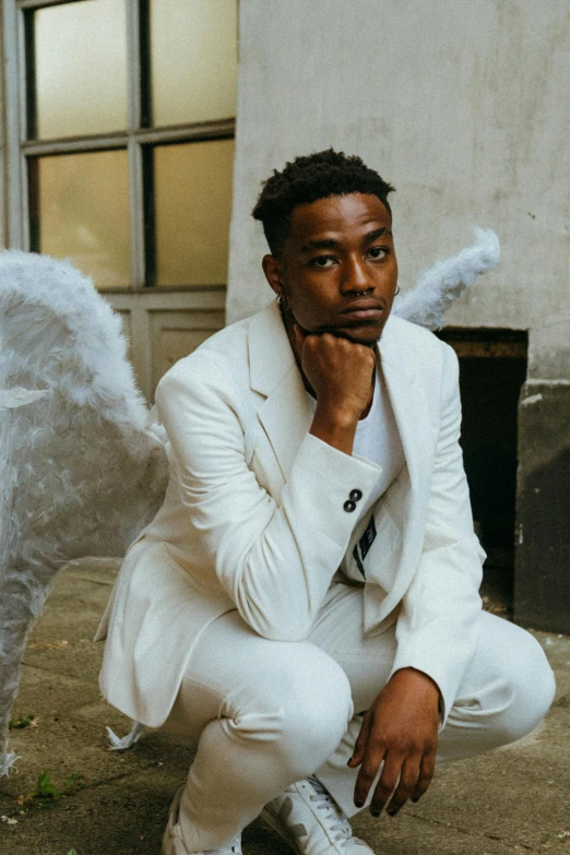 a man in a white suit and angel wings, an album cover, by Cosmo Alexander, pexels contest winner, photo in style of tyler mitchell, casual pose, sitting down, promotional image