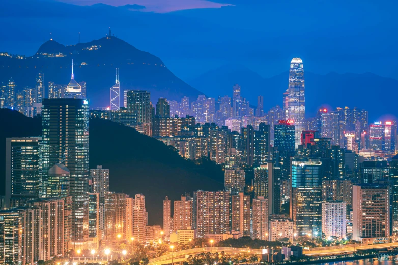 a view of a city at night with mountains in the background, city like hong kong, vibrant lights, instagram post, blue hour