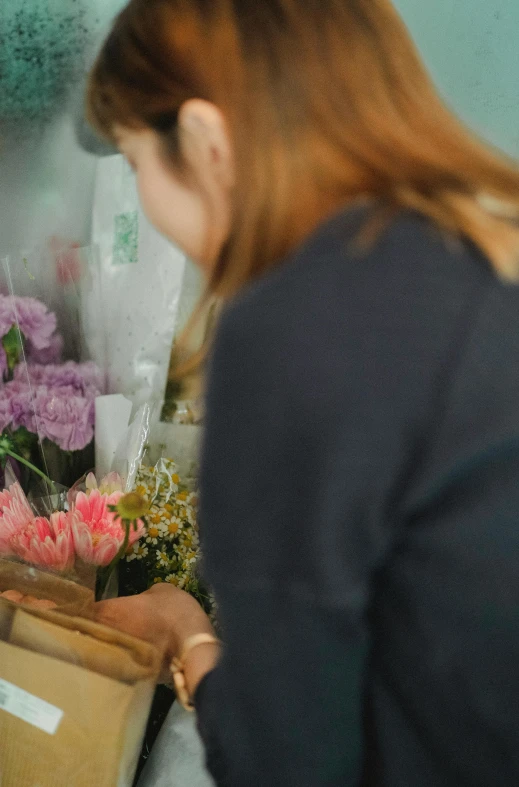 a woman standing in front of a bunch of flowers, crafting, zoomed in, shop front, at the counter