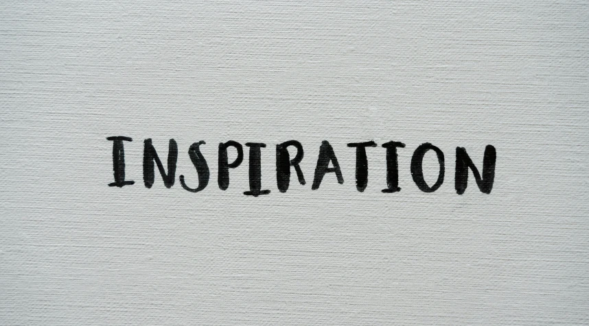 the word inspiration written in black ink on a white paper, a minimalist painting, inspired by Yamaguchi Kayo, trending on unsplash, emma bridgewater and paperchase, on a gray background, looking upward, chalk texture on canvas