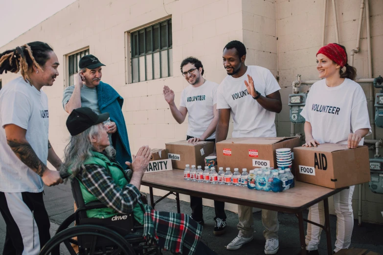 a group of people standing around a table, by Francis Helps, pexels contest winner, action bronson, effective altruism, milkboys, sitting in a wheelchair