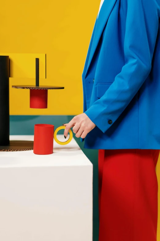 a woman in a blue jacket holding a pair of scissors, an album cover, inspired by Bauhaus, unsplash, de stijl, art toys on a pedestal, scarlet and yellow scheme, dezeen showroom, table in front with a cup