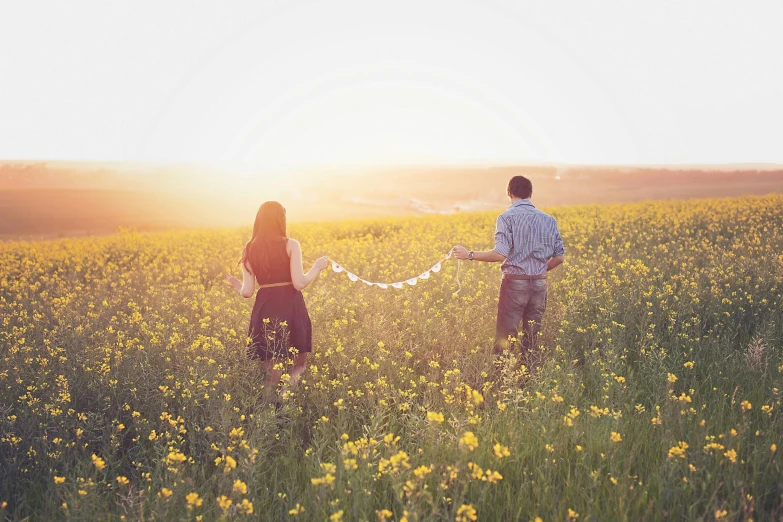 a man and a woman holding hands in a field of flowers, by Lucia Peka, pexels, yellow, day setting, instagram post, looking to the right