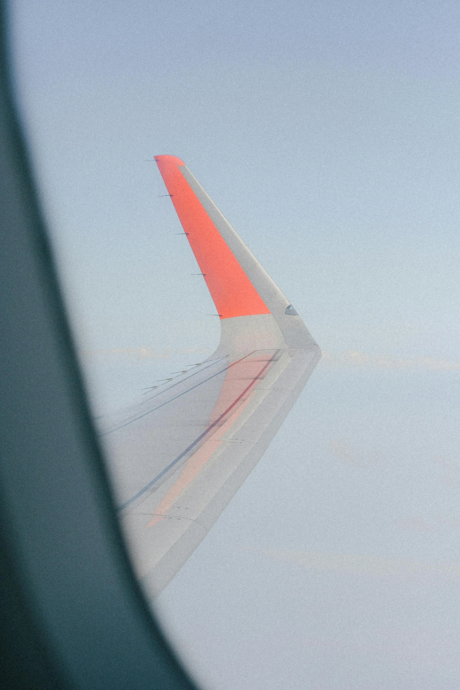 the wing of an airplane is seen through the window, by David Budd, precisionism, orange metal ears, red flag, with a sleek spoiler, taken in the late 2010s