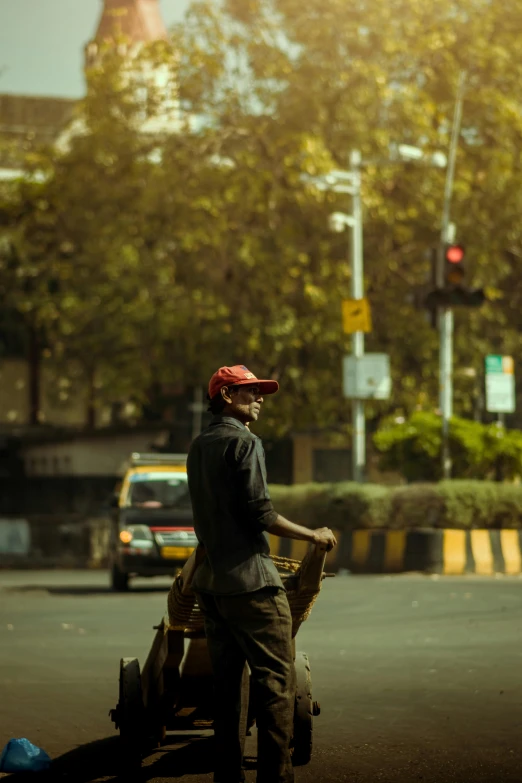 a man pushing a cart down a street, by Saurabh Jethani, he has a red hat, traffic light, low sun, portrait of tall