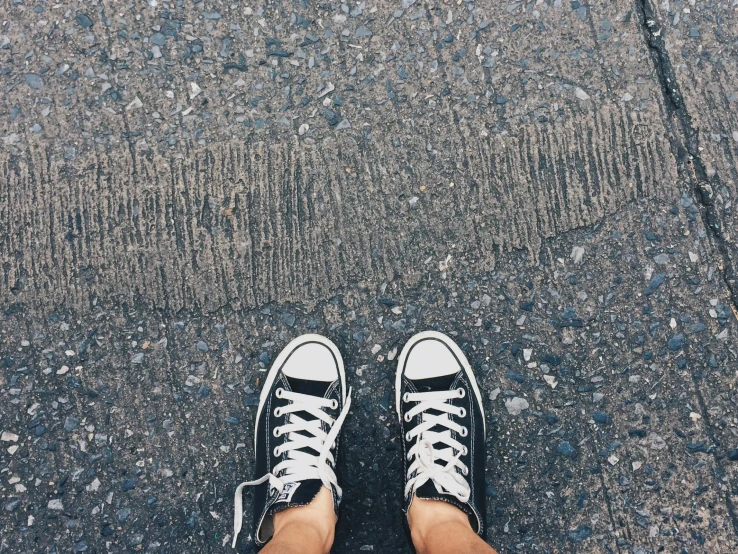 a person standing on a sidewalk wearing black and white sneakers, realism, road trip, childhood friend vibes, wide high angle view, converse