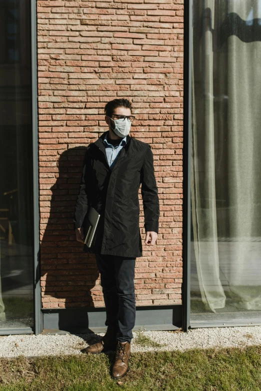 a man standing in front of a building wearing a face mask, trench coat, al fresco, profile image, neoprene