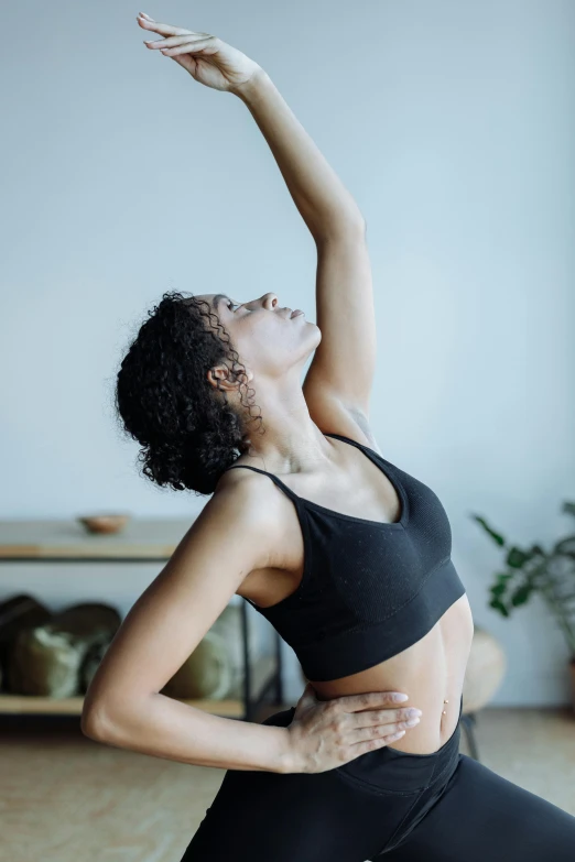 a woman doing a yoga pose on a yoga mat, by Carey Morris, pexels contest winner, arabesque, raising an arm, sport bra and shirt, looking off to the side, organic and intricate