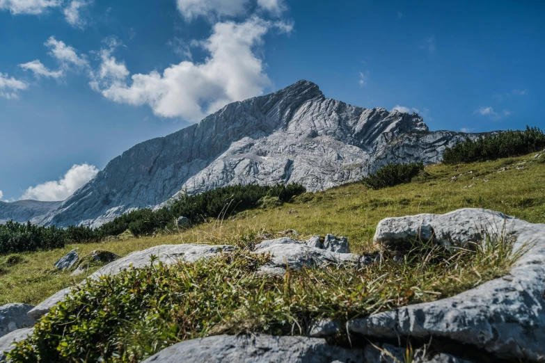 a man riding a bike on top of a lush green hillside, a picture, by Sebastian Spreng, pexels contest winner, les nabis, carrara marble, large rocky mountain, youtube thumbnail, mountain behind meadow