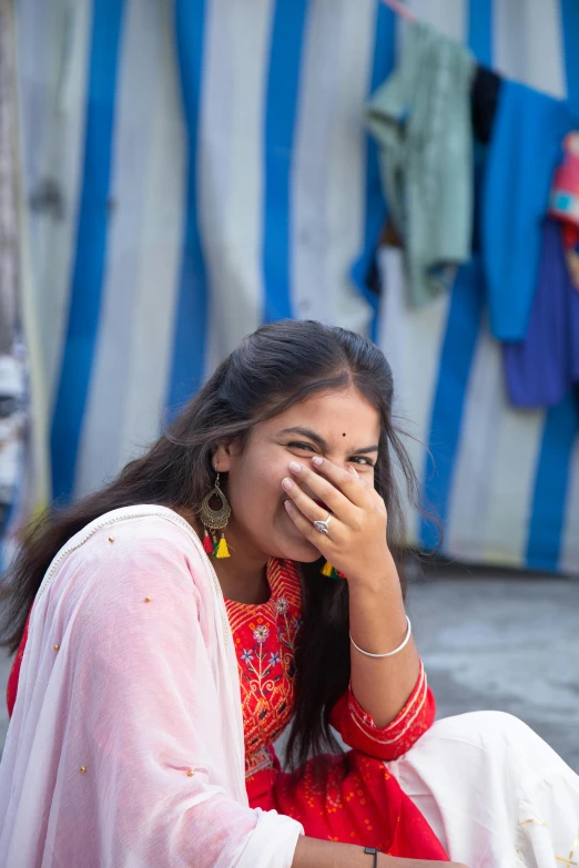 a woman sitting on the ground talking on a cell phone, pexels contest winner, dressed in a sari, earing a shirt laughing, with a covered face, teen girl