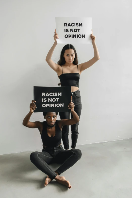 two people holding signs that say racism is not opinion, a black and white photo, trending on unsplash, feminist art, wearing a black bodysuit, instagram story, asia, ( ( brown skin ) )