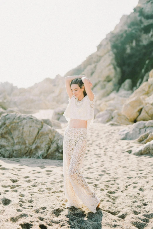 a woman standing on top of a sandy beach, white lace clothing, lulu chen, white stone arches, wearing a cropped top