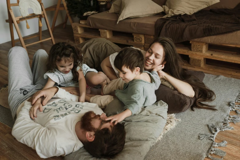 a family laying on the floor in a living room, by Adam Marczyński, pexels contest winner, 15081959 21121991 01012000 4k, cottagecore hippie, australian, playful smile