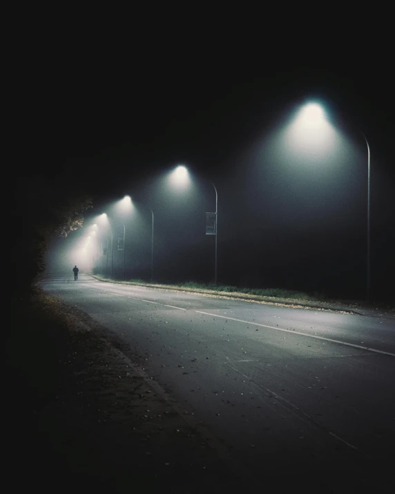 a person riding a bike down a street at night, under a gray foggy sky, empty road, streetlamps, instagram post