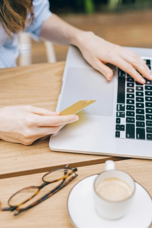 a woman holding a credit card while using a laptop, by Carey Morris, trending on pexels, private press, sitting on a mocha-colored table, website banner, dwell, photo for magazine