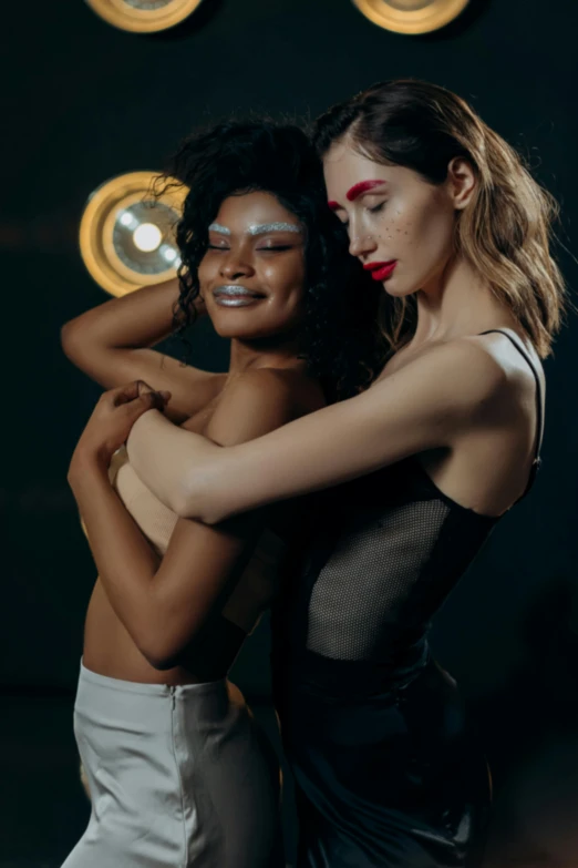 a couple of women standing next to each other, by Matija Jama, trending on pexels, renaissance, sexy girl with dark complexion, hugging, show light, nonbinary model