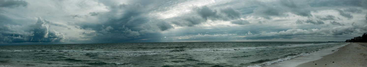 a large body of water sitting on top of a sandy beach, unsplash, stormy clouds on the horizon, high quality photo, rough seas, panorama view of the sky