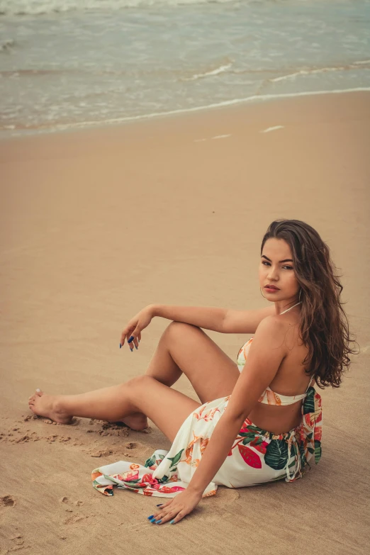 a woman sitting on a beach next to the ocean, isabela moner, elegant tropical prints, 5 0 0 px models, laying on sand