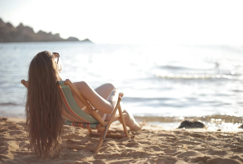 a woman sitting in a lawn chair on a beach, pexels contest winner, renaissance, girl with long hair, profile image, holiday season, sunbathing at the beach