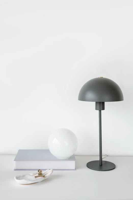 a lamp sitting on top of a table next to a stack of books, inspired by Carl Gustaf Pilo, unsplash, bauhaus, in gunmetal grey, dome, dwell, soft vignette