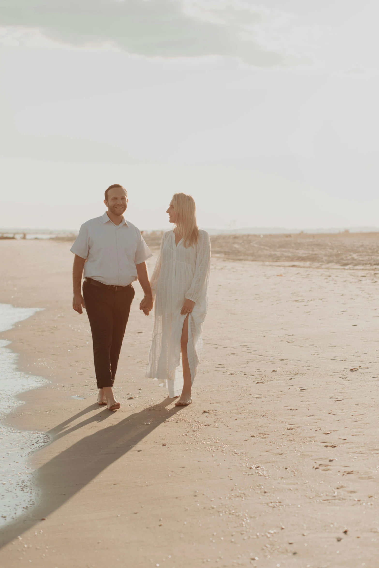 a man and a woman walking on a beach, wearing a white button up shirt, wearing simple robes, high-key, date