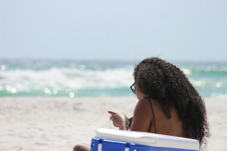 a woman sitting on top of a beach chair, by Carey Morris, pexels, black female, the emerald coast, curls, people watching around