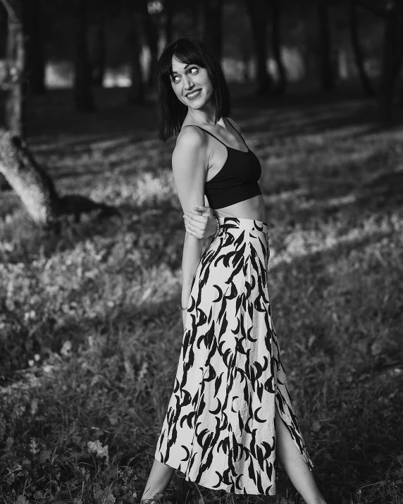 a black and white photo of a woman in a skirt, a black and white photo, by Lucia Peka, pexels contest winner, evening!! in the forest, olga kurylenko, with an elegant smile, 15081959 21121991 01012000 4k