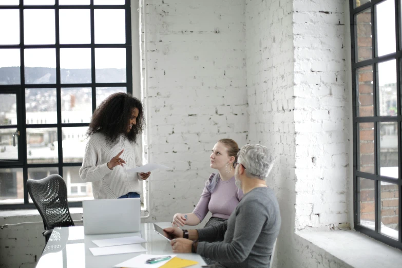 a group of people sitting around a table with laptops, by Carey Morris, pexels contest winner, white wall coloured workshop, woman holding another woman, in a meeting room, grey