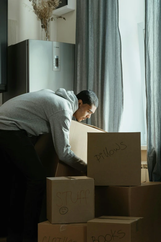 a man standing next to a pile of boxes, a stock photo, pexels contest winner, realism, bent over posture, soft lighting, apartment, ignant