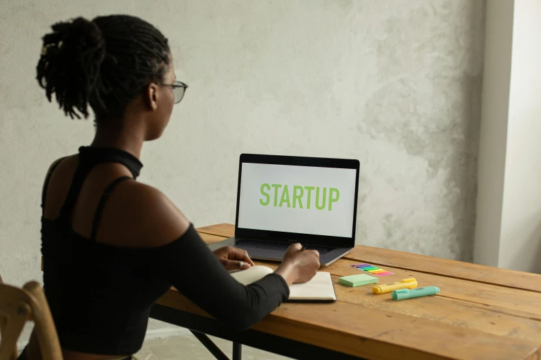 a woman sitting at a table with a laptop, trending on unsplash, graffiti, incubator medpods, wearing a crop top, ( ( dark skin ) ), ai startup